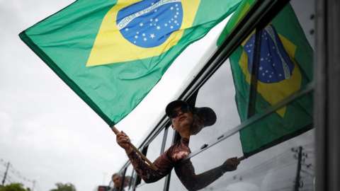 A man holds a Brazilian flag from the window of a bus as he is detained after Congress was stormed by Bolsonaro supporters
