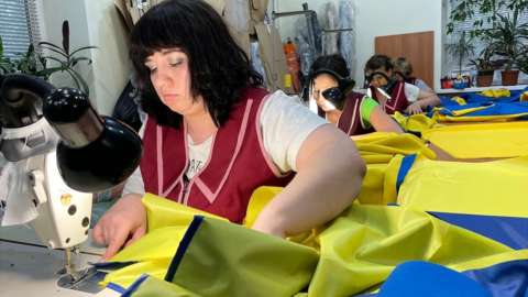 A woman sews together Ukrainian flags at a factory