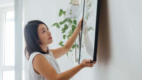 Young woman hanging picture frame on wall