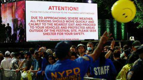 A screen shows information about severe weather approaching the area as New York police officers try to move people out of the field after cancelling the "We Love NYC: The Homecoming Concert" at Central Park
