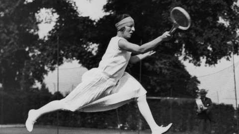 French tennis player Suzanne Lenglen wears a knee-length dress and a bandeau as she takes part in a competition in 1926.