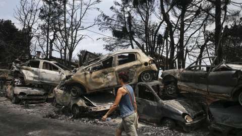 A woman walks past the burnt cars after wildfires hit the village of Mati near Athens, Greece on July 24, 2018