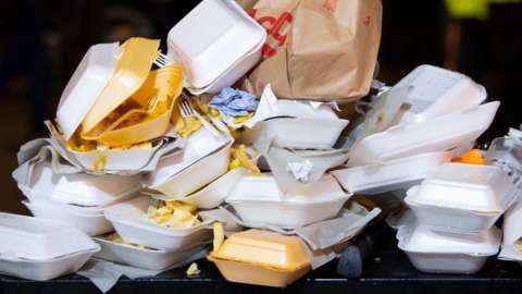 An overflowing bin full of takeaway food containers at nigh