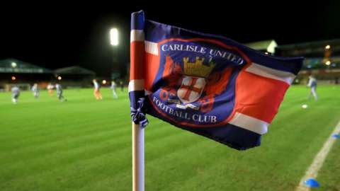 A Carlisle United corner flag with players training in the background