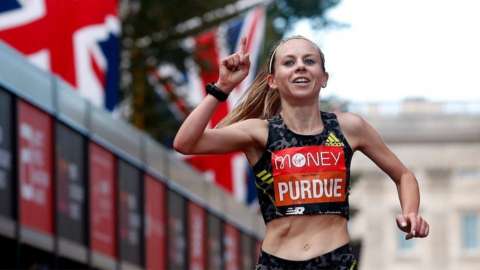 Charlotte Purdue holds up her index finger as she crosses the finish line of the London Marathon.