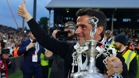 Marco Silva holding the Championship trophy gives a thumbs up gesture to the Fulham fans