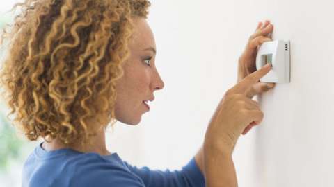 A woman uses a thermostat
