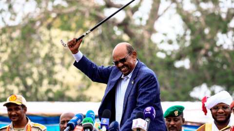 Omar al-Bashir (C) waves a walking stick as he gives a speech in Nyala, the capital of South Darfur province, on September 21, 2017