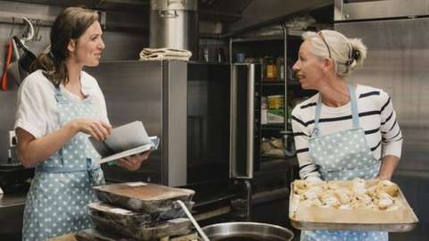 Female baker carrying a tray of fruit scones towards the worktop in the kitchen