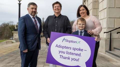 NI Health Minister Robin Swann, EJ Havlin, Director of Adoption UK, and Kathy Brownlee with her adopted son Mack Brownlee on the steps of Parliament Buildings at Stormont on Tuesday