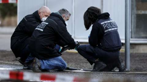 Three kneeling police officers examine a gun near the crime scene at Heidelberg University