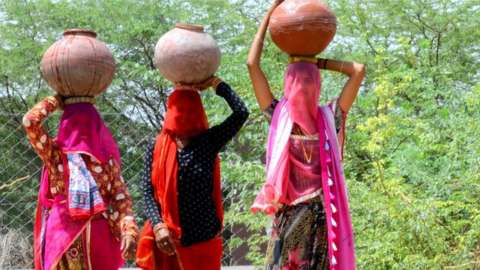 Village women carry clay pots filled with drinking water to their homes from a public tap during a hot summer day, on the outskirts of Beawar.