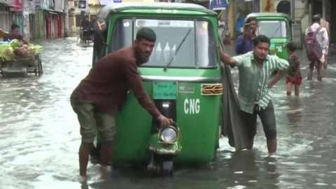 Two men push tuk tuk through flooded streets in Bangladesh