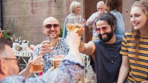 Group of mixed age friends outside holding their drinks up to toast