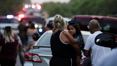 Girl holds her mother at the scene where people were found dead inside a trailer truck in San Antonio