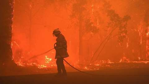 Firefigher hosing flames in bushfire