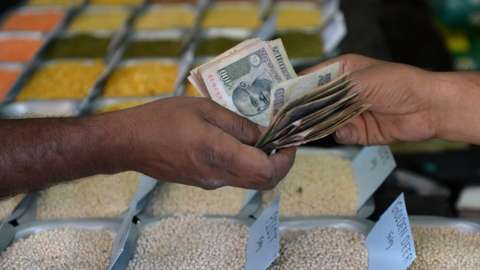 An Indian customer hands over cash to a food grain merchant at a wholesale trading shop in Bangalore