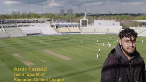 Amir Fareed sits facing camera with cricket match behind him