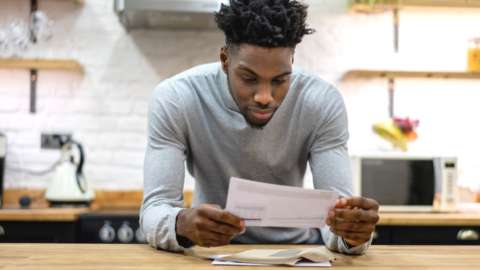 Man in kitchen looking at paper bill