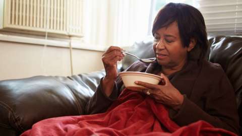Senior Woman eating soup and Keeping Warm Under Blanket - stock photo