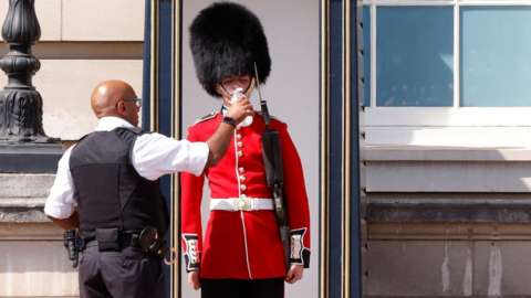 A member of the Queen's Guard receives water to drink during the hot weather, outside Buckingham Palace