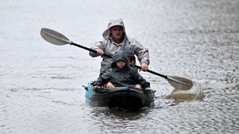 A man and a child kayak through floodwaters