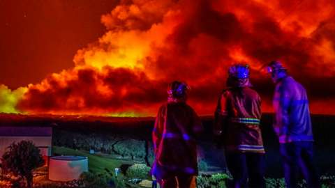 Firefighters watch massive bushfire in distance