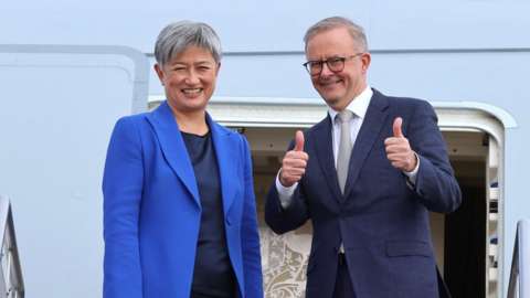 Anthony Albanese gives a thumbs up while boarding a plane beside Penny Wong