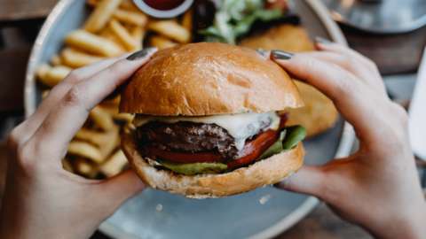 Stock image of hands holding a burger, with chips on a plate in the background