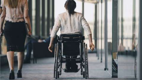 A woman who uses a wheelchair going along a corridor alongside a colleague