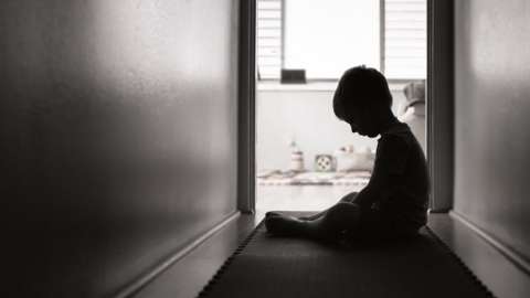 Young child sitting in a hallway with their head bowed