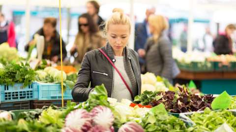 Woman at market stall browsing at tables of vegetables