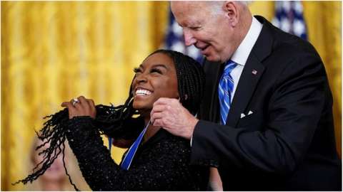 Simone Biles having the Medal of Freedom placed around he neck by President Biden.