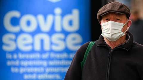 A man in a mask walks past a 'Covid Sense' sign