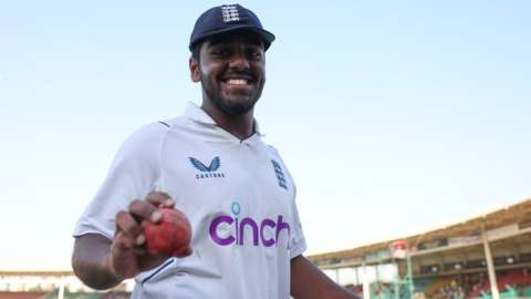 England bowler Rehan Ahmed smiles as he holds up the ball after taking five wickets on debut