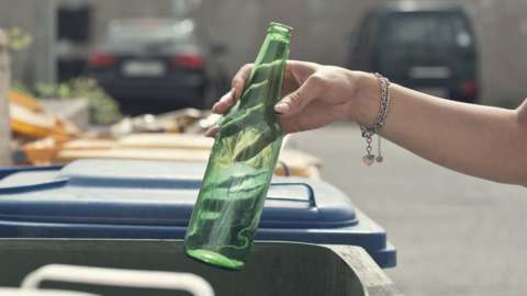 Hand placing green bottle into recyling bin
