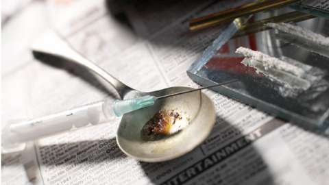 A needle and syringe with a pile of heroin on a spoon.