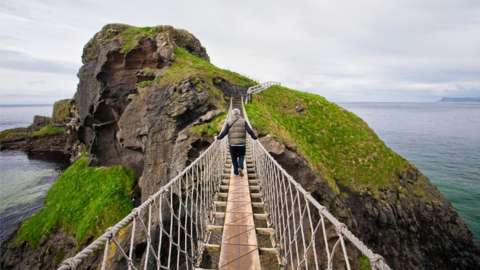 A man crossing a rope bridge towards an island in Northern Ireland.