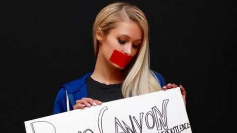 Paris Hilton with tape over mouth holding a sign