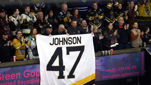 Ice hockey players tap sticks on ice in Johnson tribute