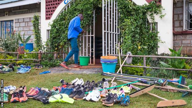 General scene of camp entrance, shoes littered on grass next to mops and brooms