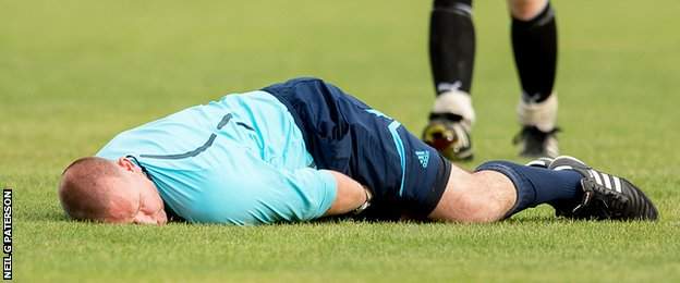 Referee Robert Baxter lies injured on the turf