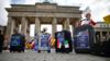 Работники туристических агентств стоят рядом с чемоданами, украшенными плакатами протеста, во время демонстрации 13 мая 2020 года перед достопримечательностью Берлина Бранденбургскими воротами