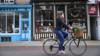 Женщина на велосипеде проезжает мимо маленьких магазинчиков в Кембридже