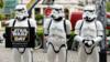 Три человека в костюмах штурмовиков из «Звездных войн» держат табличку с рекламой дня «Звездных войн»