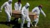 Работники кладбища носят защитные костюмы во время захоронения