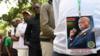 Мужчина с бейджем с фотографией покойного бывшего президента Кении Даниэля Арапа Мои стоит в очереди, чтобы осмотреть его останки