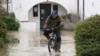 Мужчина едет на велосипеде по паводковой воде в отеле The Barn в Бедфорде