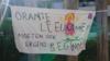 Баннер гласит: «Оранжевые львицы тоже должны где-то начинать» на игровой площадке начальной школы Де Буут
