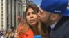 Женщина-репортер целует фанат, явно неудобно, с микрофоном DW в руке